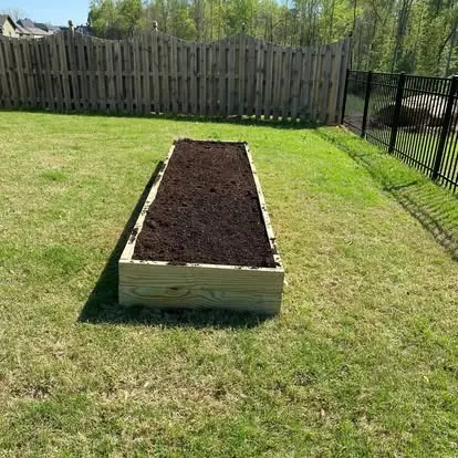 A long timber raised garden bed installed on a lawn.
