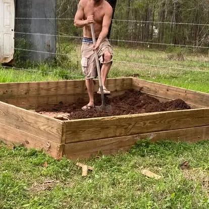 Mike Shaner working with a shovel inside a large timber raised garden bed.